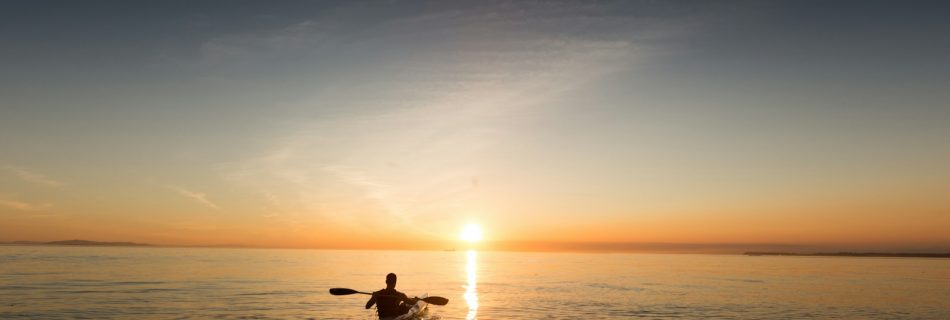 man riding kayak on water taken at sunset