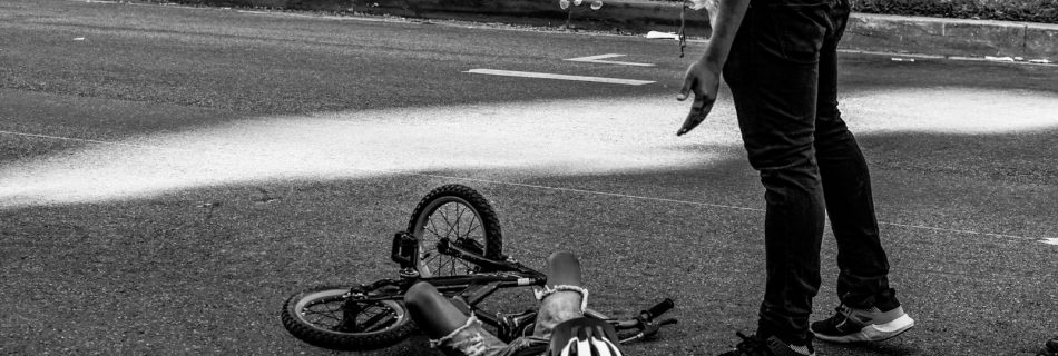 child lying on the ground beside bike and standing man