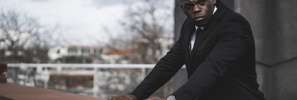 man in black suit jacket sitting on brown wooden bench during daytime