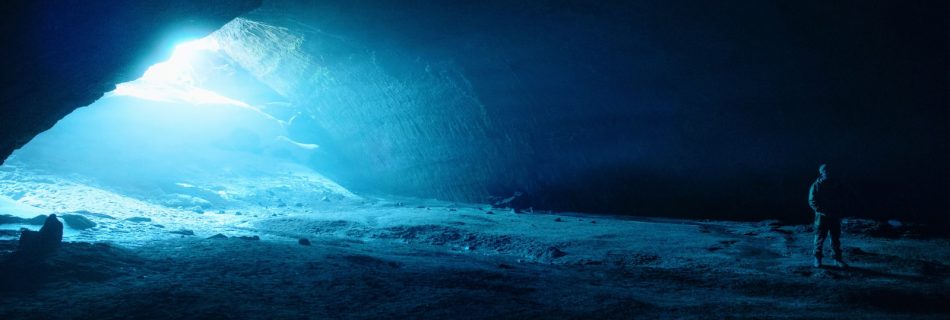 a man standing in a dark cave with a bright light coming from it